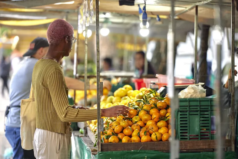 a blacked guy with a pink dyed hair in the market buying oranges